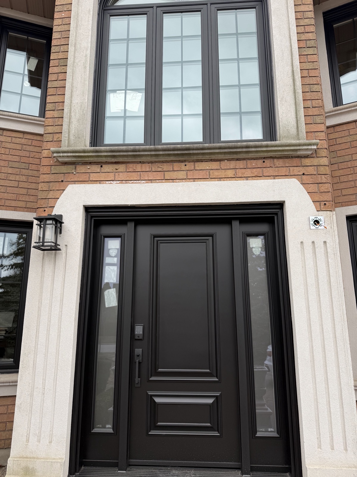 Black entry door with sidelite on a home with pale siding installed by Optima Windows and Doors in the Greater Toronto Area
